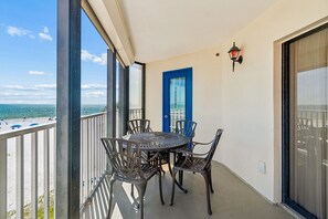 Een balkon met een ronde tafel en stoelen, een blauwe deur en uitzicht op het strand.