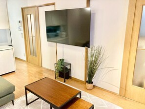 Un salon moderne avec un téléviseur à écran plat fixé au mur, une table basse en bois, un canapé gris et une plante en pot.