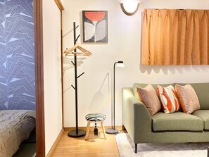 A room with a green sofa, a floor lamp, a coat rack, and a painting on the wall. - Neo Universal 04 (Osaka, Konohana, Nishikujo)