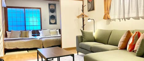 A modern living room with a sofa, a coffee table, and a bed with a view through a window.