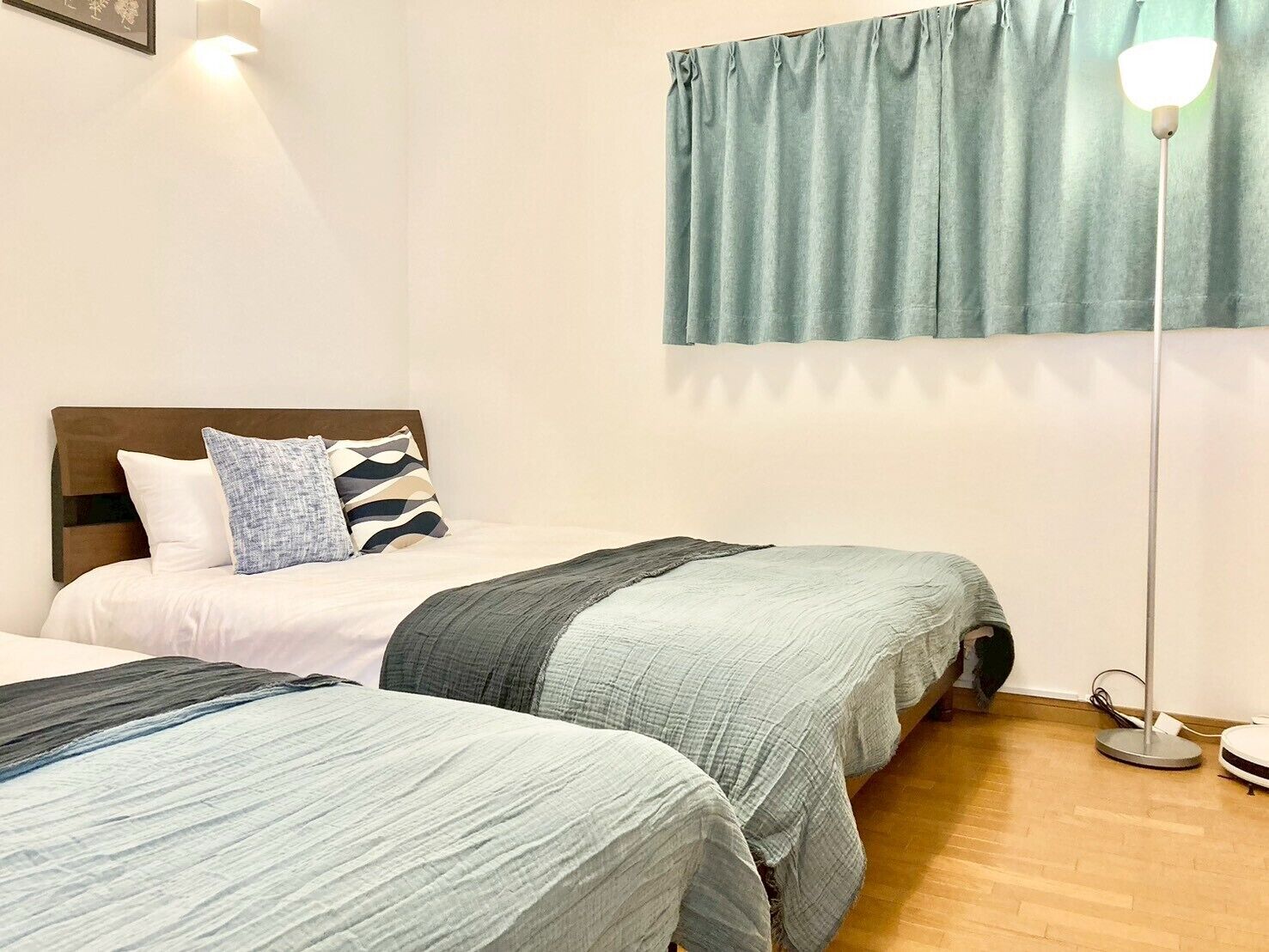Ein Hotelzimmer mit zwei Betten, einem Nachttisch, einer Stehlampe und einem Fenster mit Vorhängen.