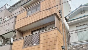 A multi-story residential building with a tiled facade, a visible entrance, and a small outdoor area with a trash bin. - Neo Universal 04 (Osaka, Konohana, Nishikujo)