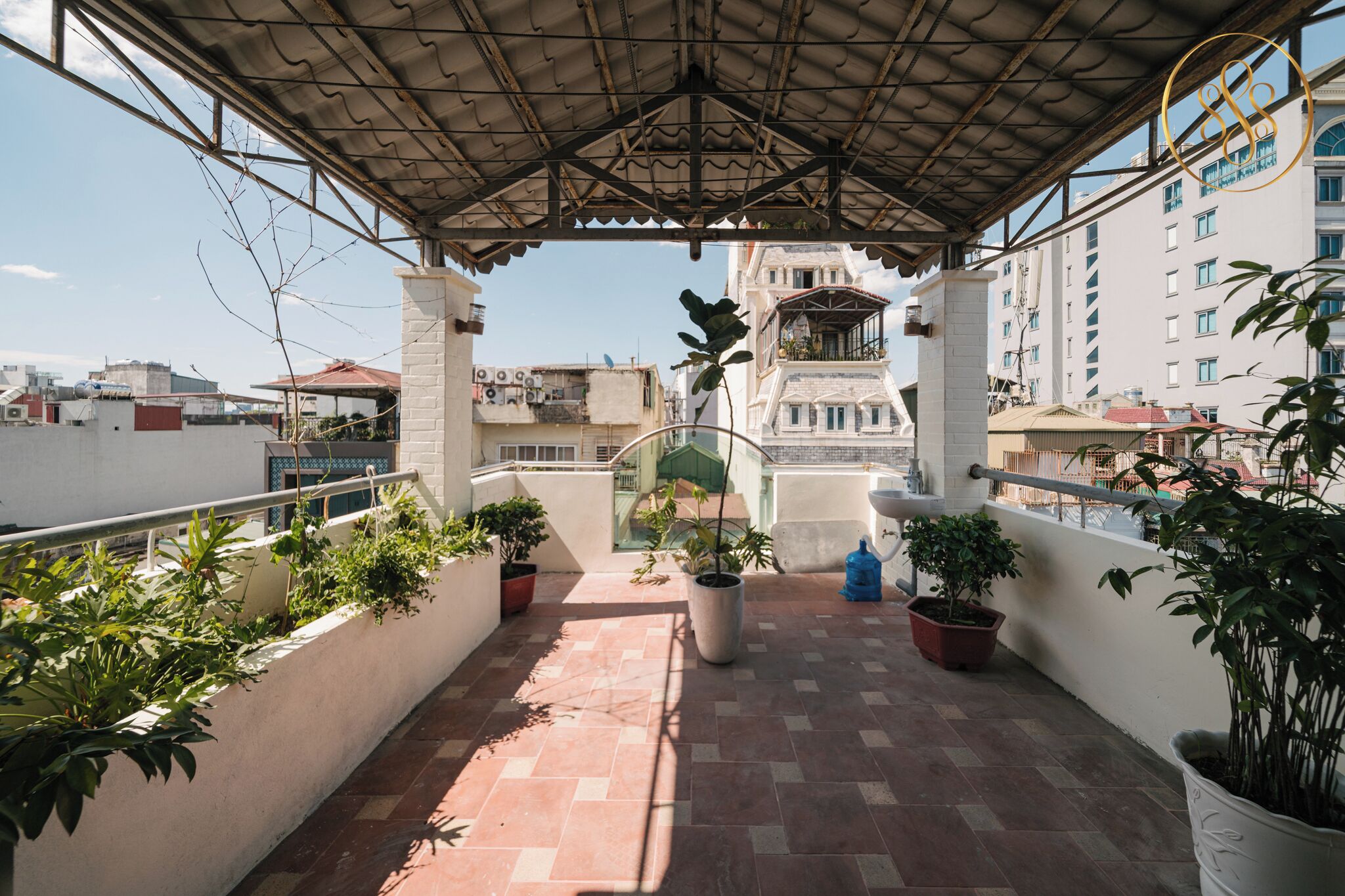 A covered outdoor area with potted plants, a fountain, and a view of buildings in the background.