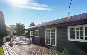 Ein Haus mit Terrasse, weißen Fensterrahmen und einem dunklen Dach.