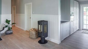A modern kitchen with white cabinetry, a black wood-burning stove, and a wicker basket on the floor. - 4 bedroom gorgeous home in Karrebæksminde (Karrebæksminde)