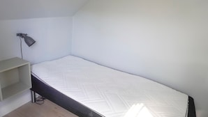 A small, single-bed room with a plain white wall, a desk with a lamp, and a simple, unadorned floor. - 4 bedroom gorgeous home in Karrebæksminde (Karrebæksminde)