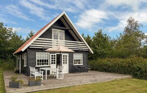 Eine Hütte mit geneigtem Dach, einer Veranda mit Sitzgelegenheit und einer Holzterrasse.