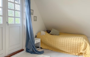 Ein Schlafzimmer mit Bett, Nachttisch, Fenster mit Vorhängen und einer Tür.