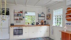Keittiössä on valkoiset kaapit, sisäänrakennettu uuni, pesuallas ja ikkuna, jossa on sälekaihtimet.