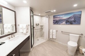 Een moderne badkamer met een marmeren wastafel, een douchecabine van glas, een toilet en een schilderij van een berglandschap aan de muur.