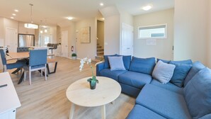 A modern living room with a blue sofa, a round coffee table, and a dining area with a table and chairs. - 4BR Cozy Home in  Calgary with Hot Tub (Calgary)