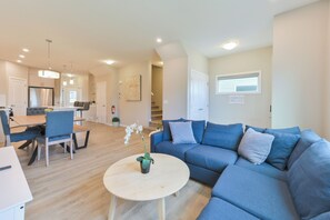 Ein modernes Wohnzimmer mit einem blauen Sofa, einem runden Couchtisch und einem Essbereich mit Tisch und Stühlen.