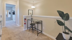 A hallway with beige walls, a black metal table with a stool, a potted plant, and a framed picture on the wall. - 4BR Cozy Home in  Calgary with Hot Tub (Calgary)