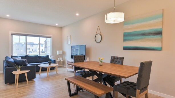 A modern living room with a sofa, coffee table, dining table, and chairs. There is a TV, a painting, and a window with a view of buildings. - 4BR Cozy Home in  Calgary with Hot Tub (Calgary)