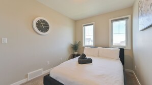 A bedroom with a bed, a wall clock, two windows, and a potted plant. - 4BR Cozy Home in  Calgary with Hot Tub (Calgary)
