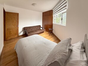 Een slaapkamer met een bed, een bank, een raam en een houten vloer.