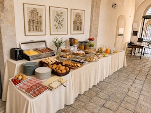 A buffet table with various food items and a coffee station, set in a room with stone walls and framed pictures on the wall.