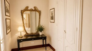 A hallway with a black console table, a large ornate mirror, a potted plant, and a white door with a decorative panel.