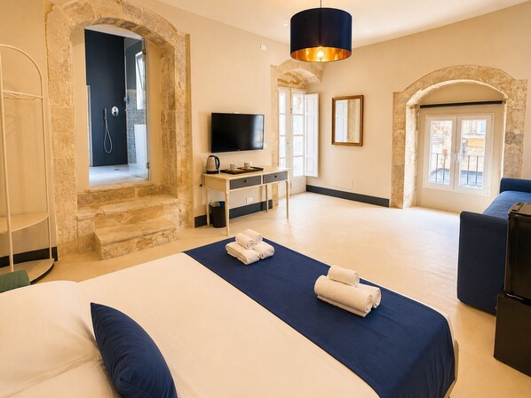 A hotel room with a bed, a desk, a television, and stone walls.