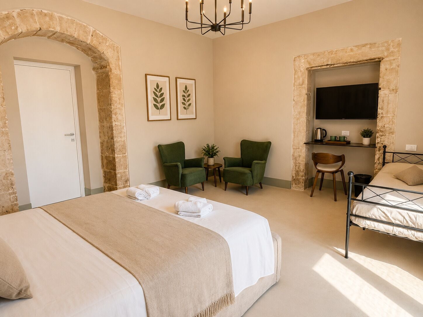Una habitación de hotel con una cama, dos sillones verdes, una mesita con una planta, un televisor fijado en una pared de piedra y una puerta.