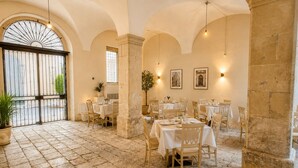 A restaurant with stone flooring, white tables, and chairs, featuring arched ceilings and wall-mounted lighting.