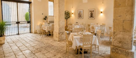Un restaurante con suelo de piedra, mesas y sillas blancas, techos abovedados e iluminación empotrada en la pared.