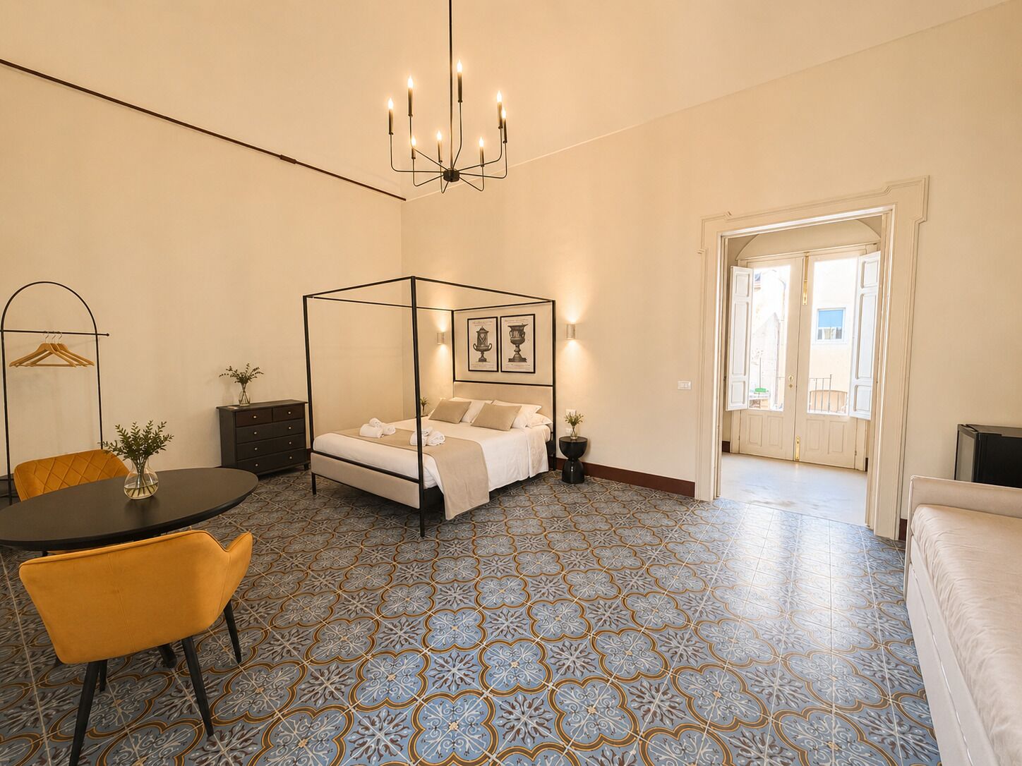 Un dormitorio con cama con dosel, una araña, una mesa de comedor con sillas y baldosas de suelo estampadas.