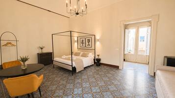 Un dormitorio con cama con dosel, una araña, una mesa de comedor con sillas y baldosas de suelo estampadas.