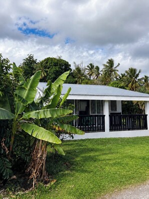 A white building with a black railing, surrounded by lush greenery and palm trees. - ‘Ūtū Retreat 
 a peaceful open-plan studio designed for rest (Avarua)