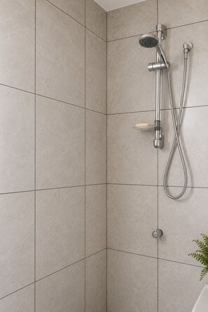 A shower with a handheld showerhead and a wall-mounted faucet, set in a tiled bathroom. - ‘Ūtū Retreat 
 a peaceful open-plan studio designed for rest (Avarua)