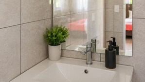 A modern bathroom with a large mirror, a white sink, and a potted plant. - ‘Ūtū Retreat 
 a peaceful open-plan studio designed for rest (Avarua)