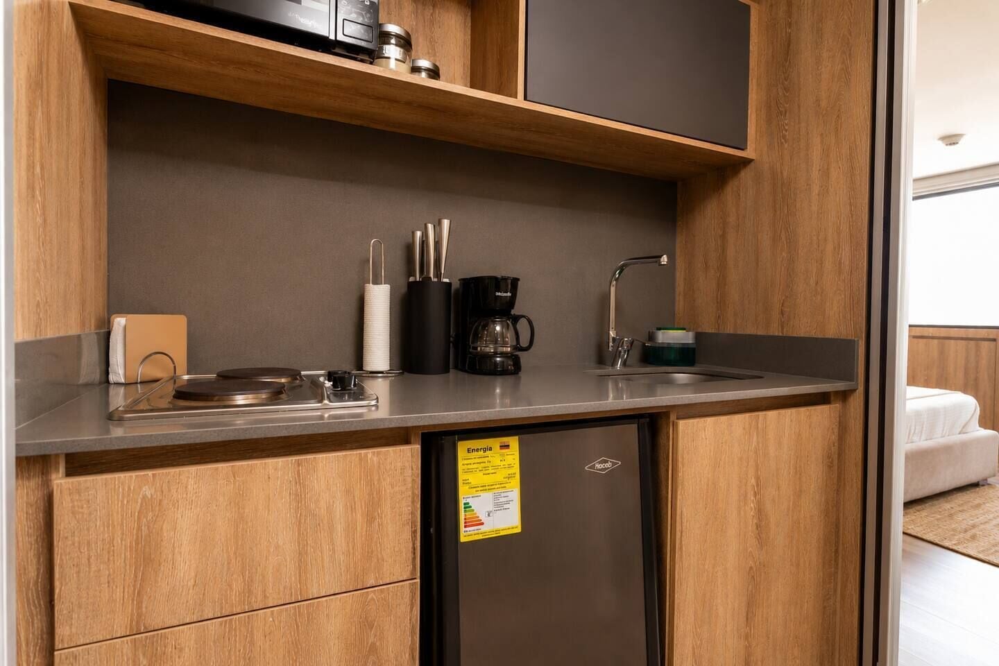 Una kitchenette compacta con un lavamanos de acero inoxidable, una cafetera y un refrigerador pequeño.