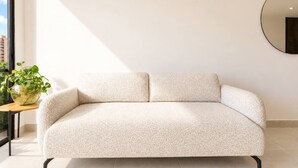 Un soggiorno minimalista con un divano chiaro, uno specchio rotondo appeso e un tavolino con una pianta.