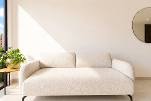 Ein minimalistisches Wohnzimmer mit einem hellen Sofa, einem runden Spiegel an der Wand und einem kleinen Tisch mit einer Pflanze.