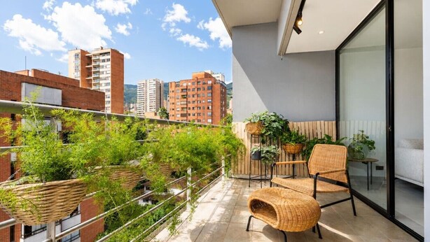 Un balcone con mobili in vimini, piante in vaso e vista sulla città.