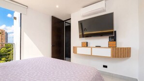 Una camera da letto con un letto, una TV a muro e un balcone con vista sugli edifici.