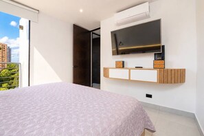 Ein Schlafzimmer mit Bett, einem an der Wand montierten Fernseher und einem Balkon mit Blick auf Gebäude.
