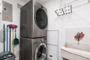 Ein kleiner Waschraum mit einer übereinander angeordneten Waschmaschine und einem Trockner, einem Wäscheständer und verschiedenen Reinigungsmitteln.