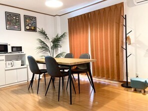 A dining area with a wooden table and four chairs, a plant, a coat rack, and a microwave on a shelf. - Neo Universal 05 (Osaka, Konohana, Nishikujo)