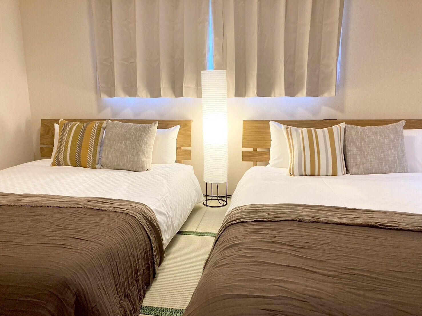A hotel room with two beds, a large window with curtains, and a tall floor lamp.