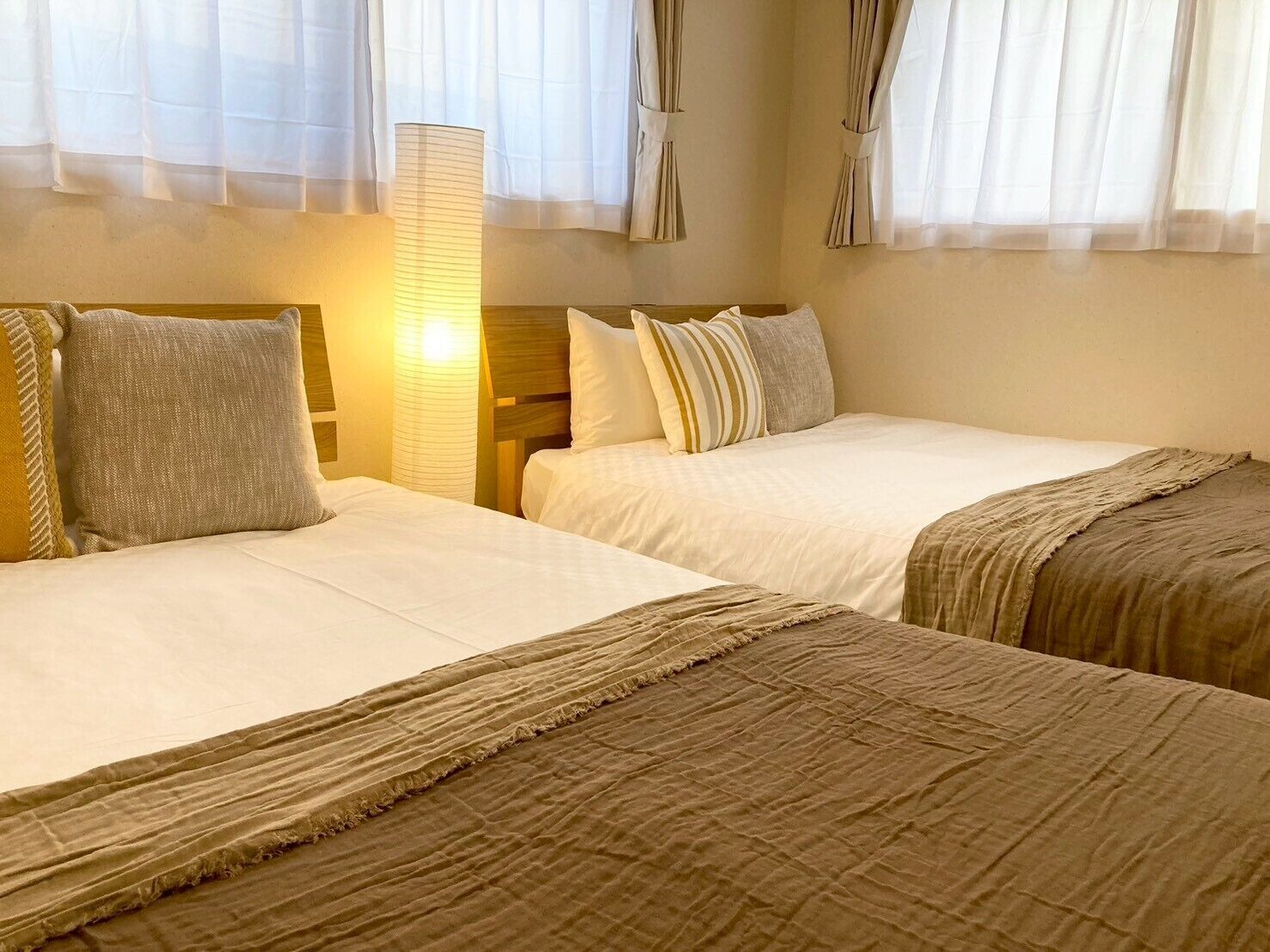 A hotel room with two beds, a nightstand, and a lamp.