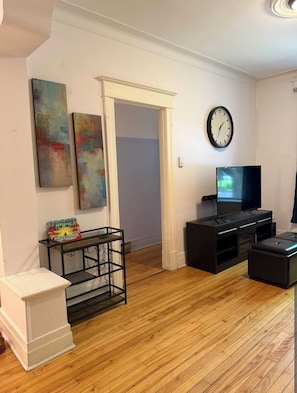A living room with a wooden floor, a television, a black entertainment unit, and abstract paintings on the wall. - Verdun Beach House (Montréal)