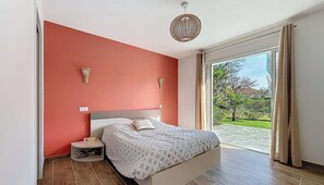 A bedroom with a bed, a nightstand, a wall-mounted lamp, and a view of a garden through a sliding door. - Villa nestled between the mountains and the Basque Country (Sauvagnon)