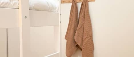 Un lit superposé avec une structure en bois et une literie blanche, une étagère en bois avec une serviette marron, et un plancher en bois.