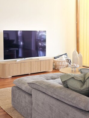 A living room with a flat-screen TV, a sofa, a coffee table, and a small side table with bottles.