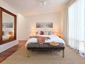 Un dormitorio con una cama grande, lámparas de noche, un espejo y vistas al exterior.