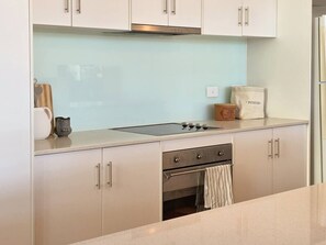 A modern kitchen with a stainless steel stove, a light blue backsplash, and a bag of potatoes on the counter. - Villa #60 South Shores ~ relaxed coastal holidays (Normanville)