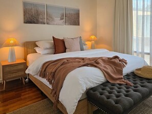 A bedroom with a bed, bedside lamps, a bedside table, and a view of the outdoors. - Villa #60 South Shores ~ relaxed coastal holidays (Normanville)