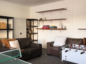A living room with two sofas, a foosball table, and shelves with books and decorative items. - Villa #60 South Shores ~ relaxed coastal holidays (Normanville)