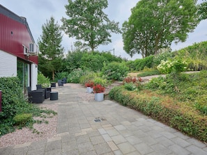 Een geplaveid pad dat leidt naar een gebouw met een rood dak, omgeven door weelderige begroeiing en verschillende planten.